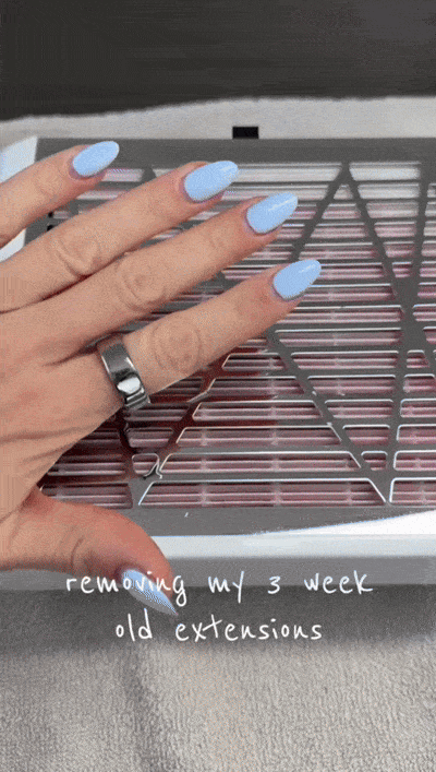 Hand with blue almond nails over a nail dust collector while filing off old extensions